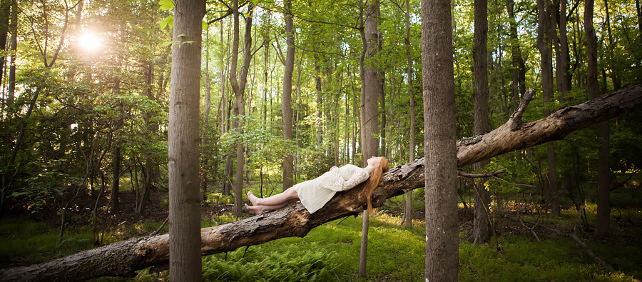 High school senior wearing white dress laying on fallen tree in south jersey woods